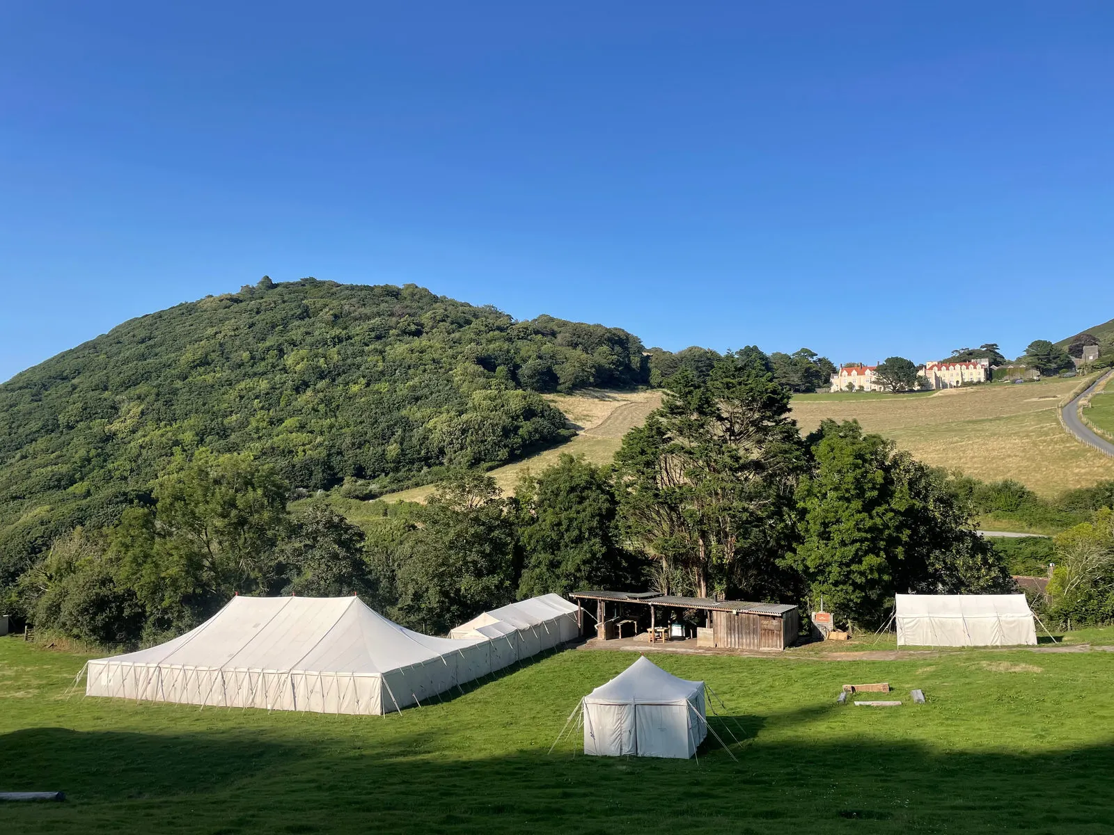 Marquees pitched in a valley beneath a wooded Devon hill