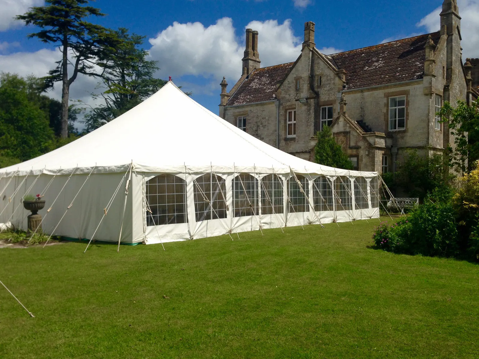 White traditional pole marquee pitched beside a gothic stone manor house