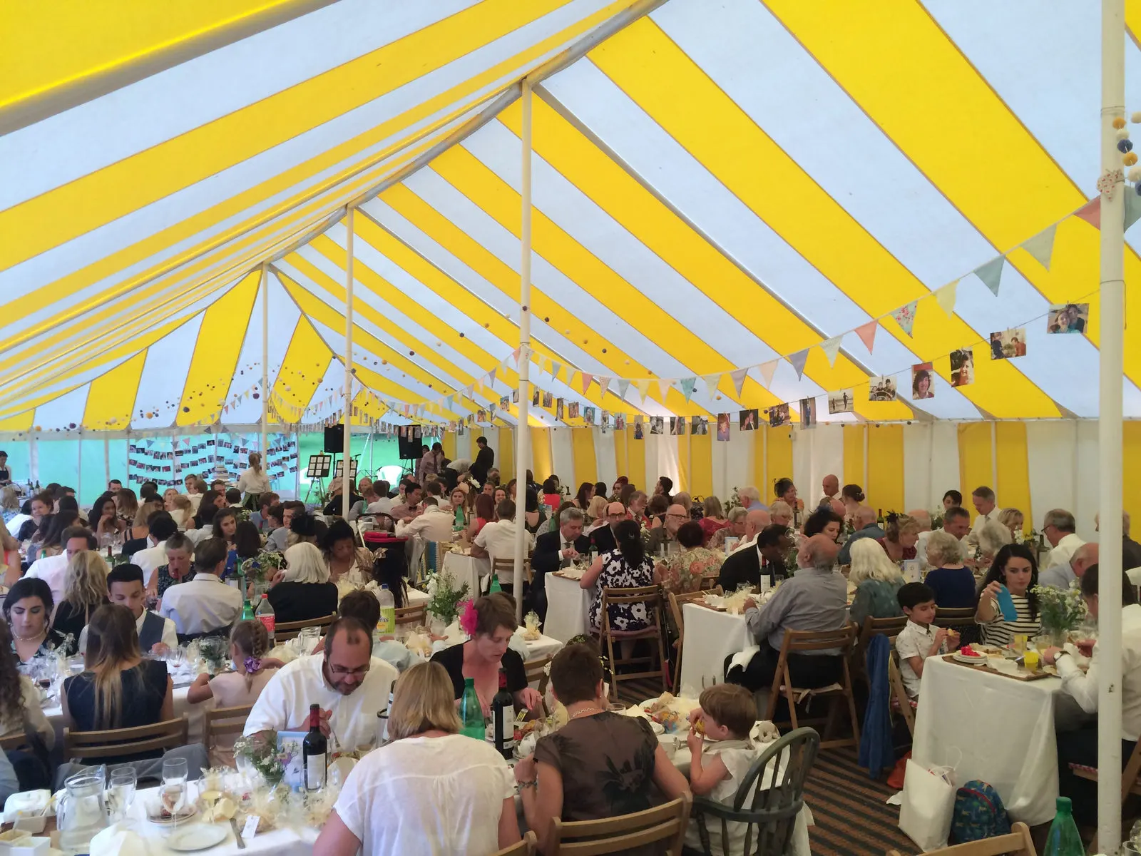 Guests dining under a yellow and white striped marquee decorated with bunting