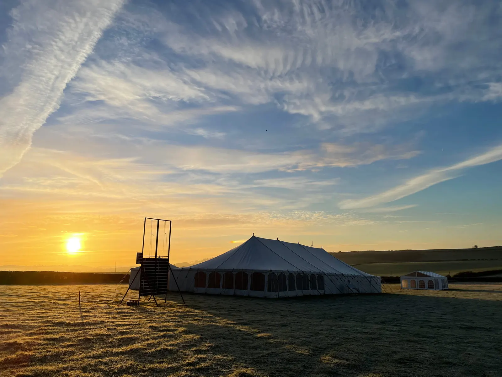 A traditional pole marquee pitched in a Dorset field at sunset